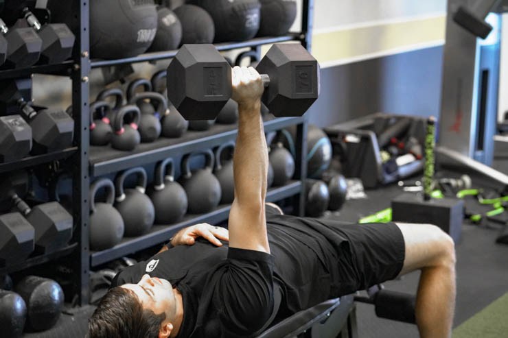 Someone holding a 70-pound REP Fitness Dumbbell while laying on a bench. 