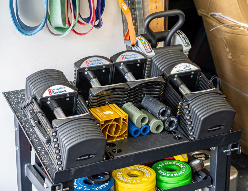 A rack in a garage gym holding PowerBlock Adjustable Dumbbells