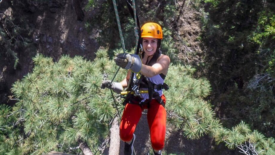 A woman rappelling in a helmet, gloves, and red leggings