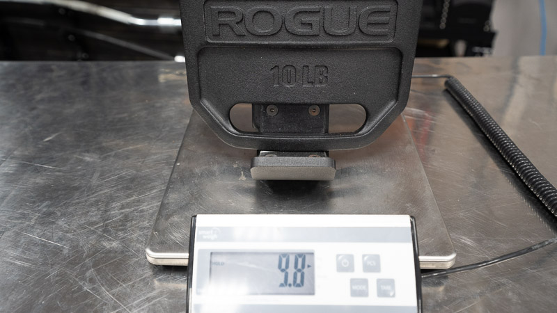 Testing the accuracy of a Rogue 10 lb. weighted vest plate on a scale, with the screen reading 9.8 lbs.