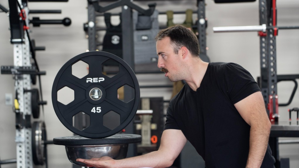 A man displays a REP Equalizer Urethane-Coated Plate on a weight plate and chalk bucket