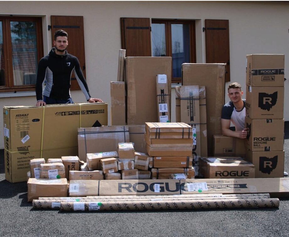 two people standing with a large shipment of Rogue fitness equipment still in shipping boxes