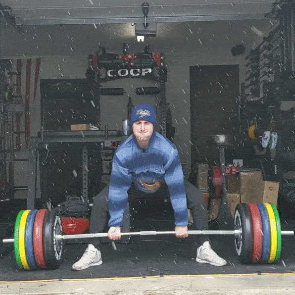 man deadlifting heavy barbell in garage gym during snow storm