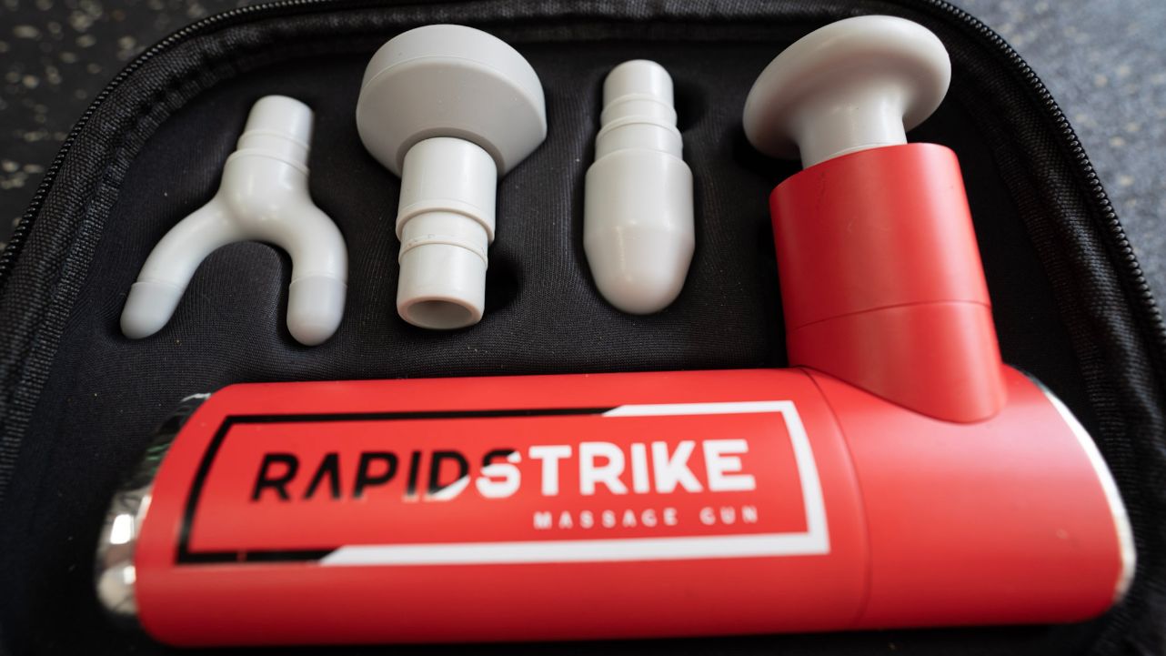 Closeup of the REP Rapidstrike massage gun in its carrying case with the four attachment heads