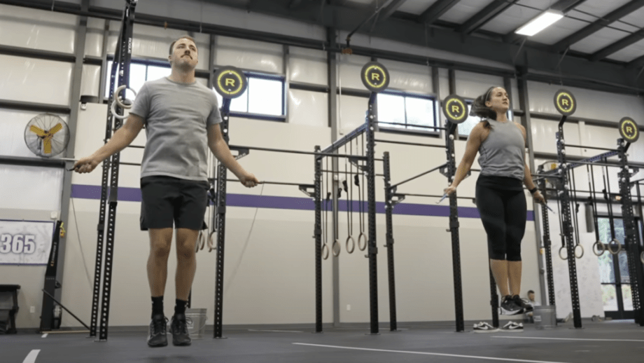 Action shot of a man and a woman jumping rope in a large gym.