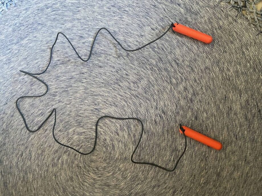 Overhead view of the black Tangram Smart Rope Rookie Jump Rope with bright orange 5-inch long plastic handles, emphaizing the lightweight cable.