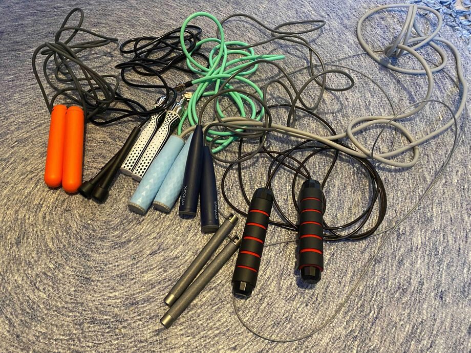 Overhead view of a jumbles pile of jump ropes with variations of handle colors and textures, and differing cable weights and materials.