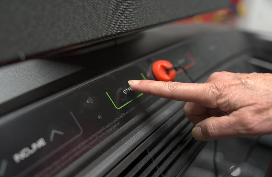 A senior's hand interacts with the console of a Nordictrack Commercial 2450 treadmill