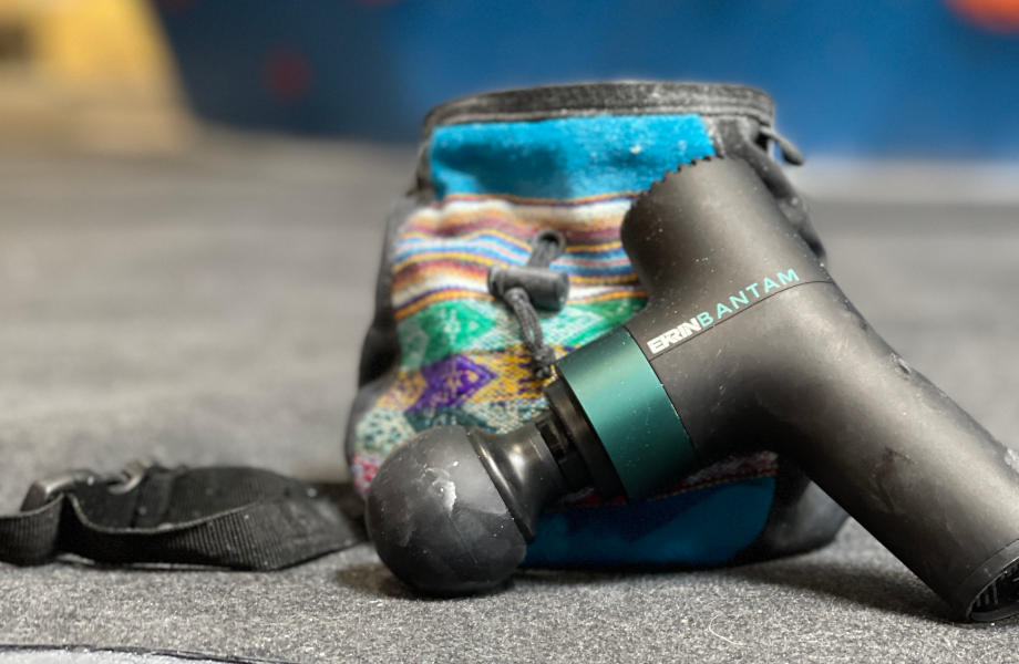 An Ekrin Bantam mini massage gun rests against a person's bag.