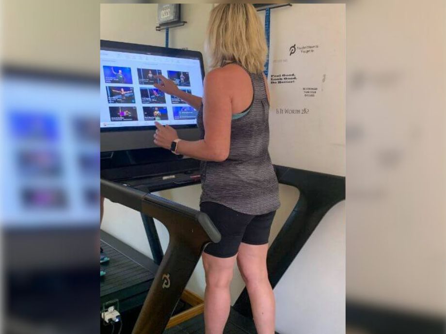 A person in shorts and a tanktop using the touchscreen of a Peloton Tread