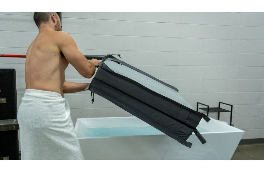 Man with a white towel around his waist putting the cover on a cold plunge tub