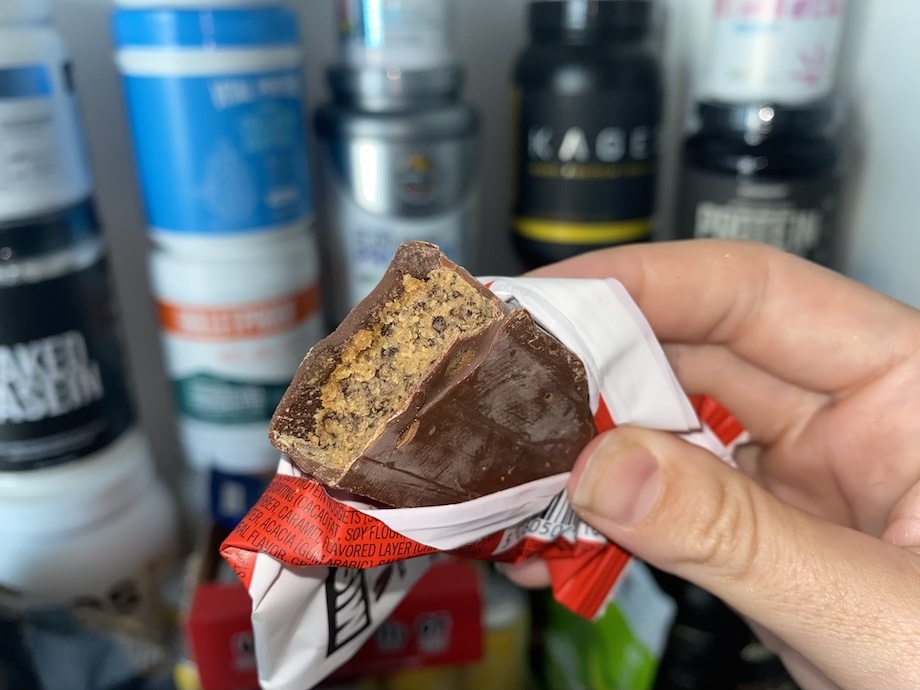 A hand holds a MisFits Plant-Powered Protein Bars in front of a stack of supplements
