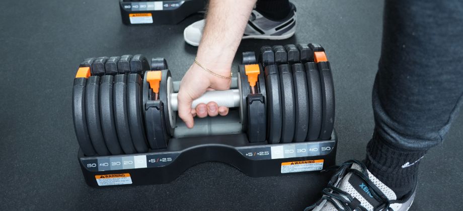 Person grabbing the NordicTrack Adjustable Dumbbells out of the plastic cradle