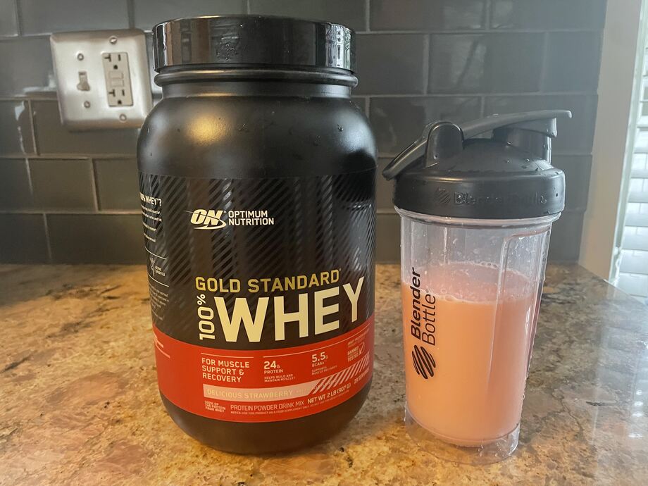 A container of Optimum Nutrition Gold Standard Whey Protein Powder next to a shaker cup filled with a protein shake