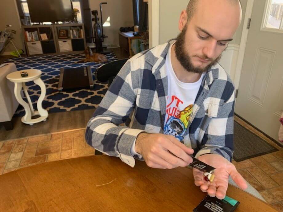 A man sitting at a table and pouring an Onnit Total Human packet of supplements out into his hand.