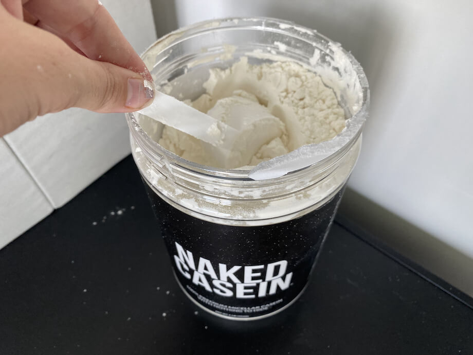 A person taking a scoop from a container of Naked Nutrition Micellar Casein