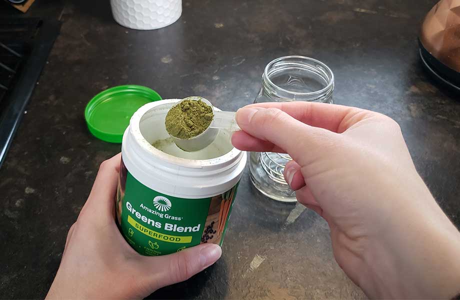 amazing grass greens superfood being scooped into a mason jar. The powder has a few lumps in it 