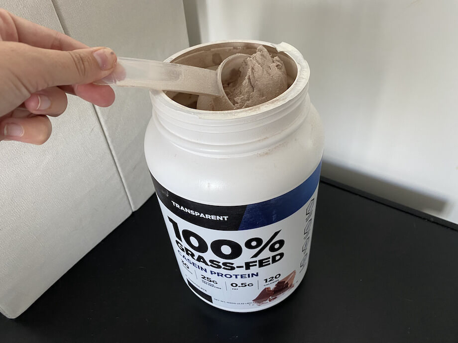 A hand scooping Transparent Labs Casein Protein out of the container