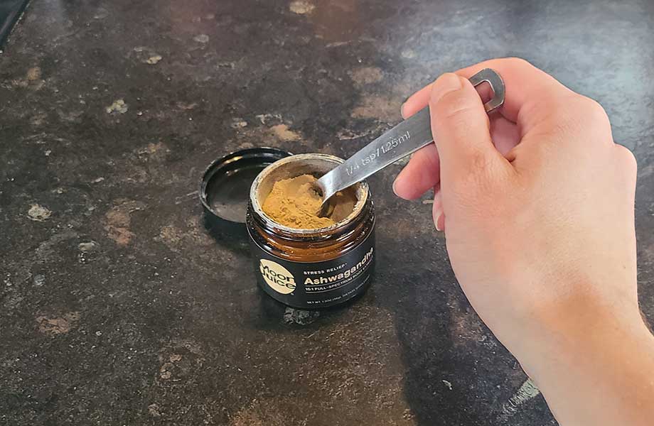 A person scoops a bit of Moon Juice Ashwagandha Powder out of its container