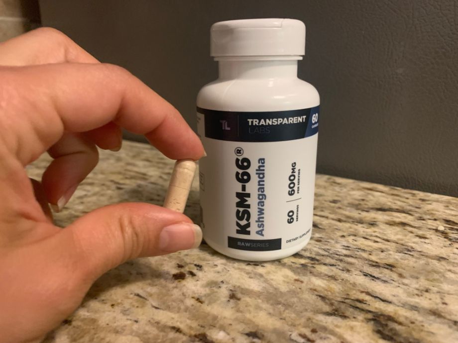 A person holding a single pill in front of a bottle of Transparent Labs Ashwagandha