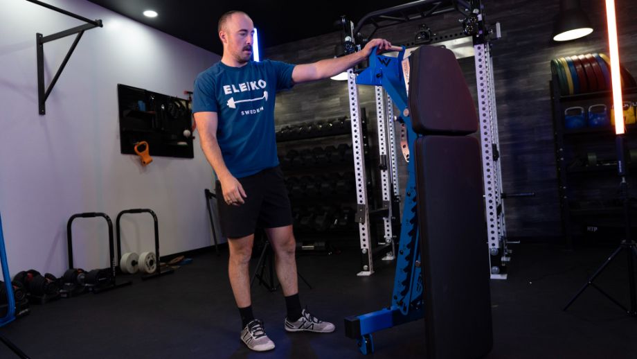 Man in a gym showing how the REP Blackwing weight bemch can be stored vertically