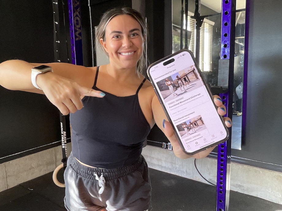 A smiling woman points to the Centr app on her upheld smartphone.