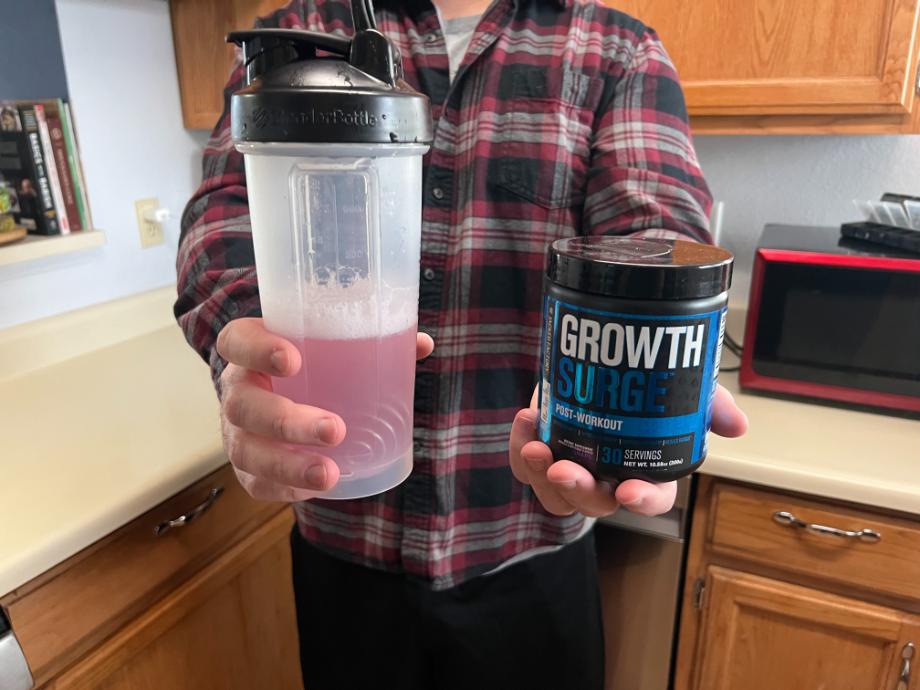 A man holds up a shake in one hand and a container of Jacked Factory Growth Surge in the other hand.