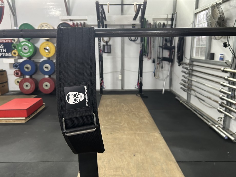 A Gymreapers Quick-Lock Belt is shown hanging from a bar in a gym.