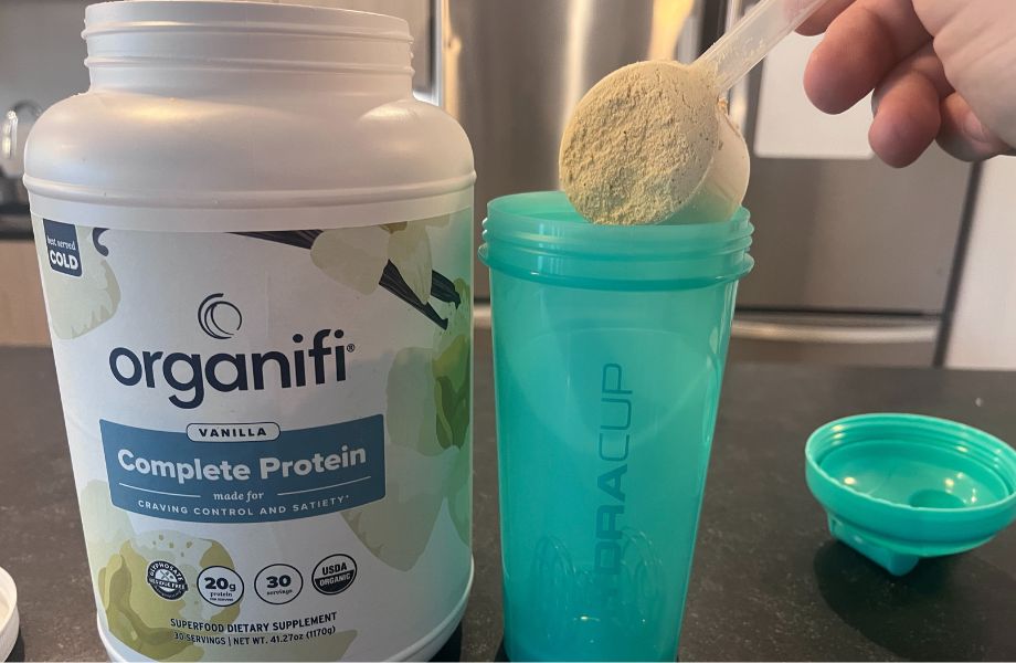 Person scooping Organifi protein powder into a blender bottle