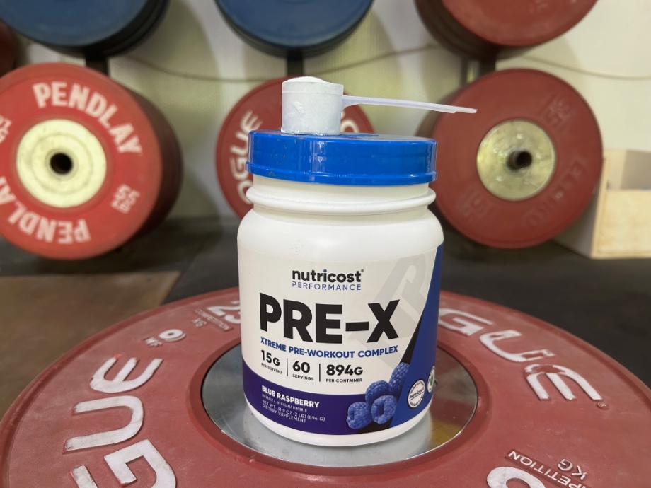 Nutricost Pre-X Pre-Workout container and scoop on top of a weight plate