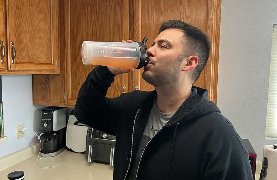 A man is shown drinking a dose of El Jefe Pre-Workout, an orange liquid in a clear shaker bottle