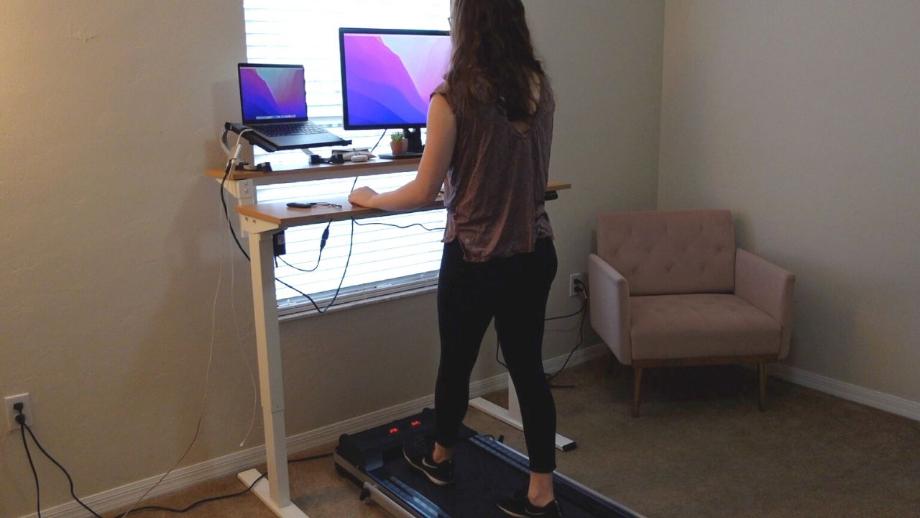 A woman is shown using the Redliro Under Desk Treadmill while working at a standing desk.