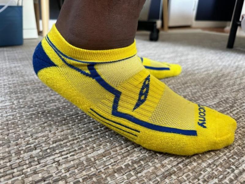 A close-up image of a person's foot wearing the bright yellow and navy blue Saucony Bolt Rundry Performance No Show Socks