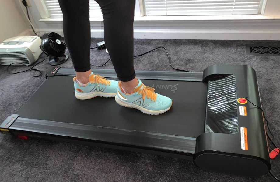 A person's feet is shown walking on the Sunny Health and Fitness Under-Desk Treadmill