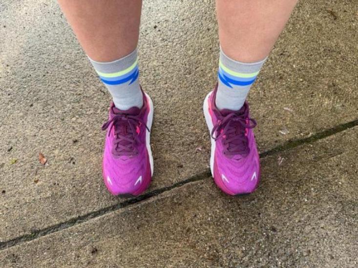 A person wearing purple running shoes paired with the Feetures Elite Light Cushion Mini Crew Socks in grey with neon yellow and blue bands