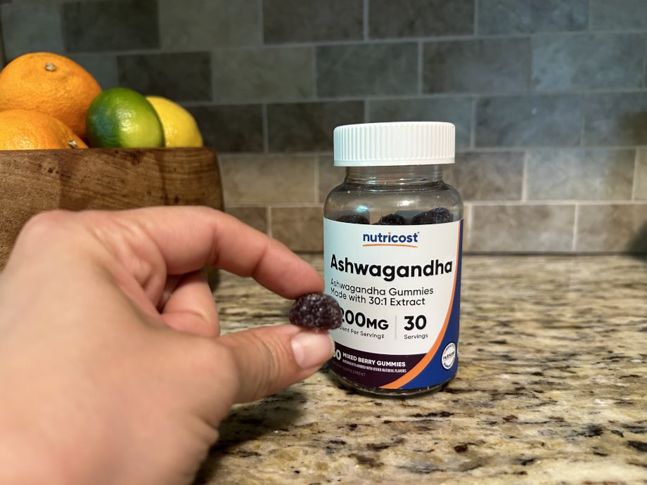 A hand holds up a gummy from a bottle of Nutricost Ashwaganda Gummies