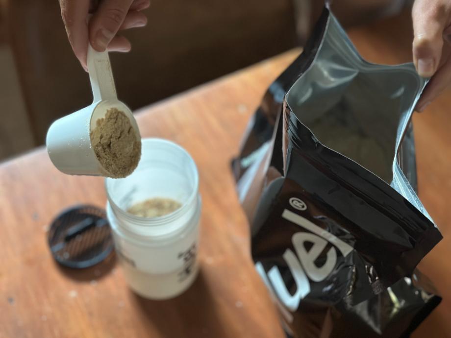 A person pouring a scoop of Huel Black Edition into a shaker bottle