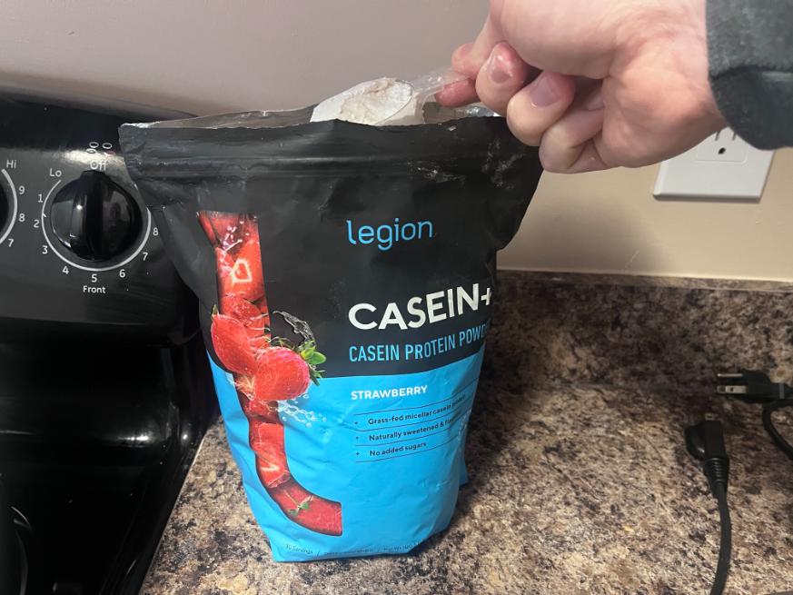 A hand scoops up some Legion Strawberry Casein powder.