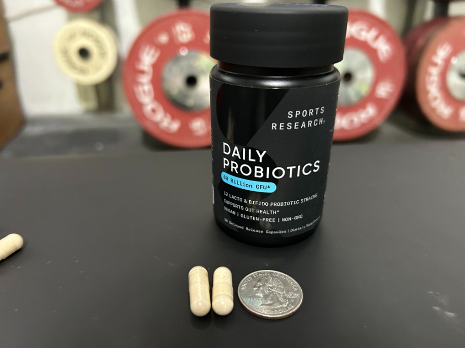Two capsules of Sports Research Probiotic laying next to a quarter for a size reference.