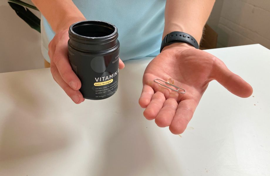 Person holding bottle and one softgel of Sports Research Vitamin D 