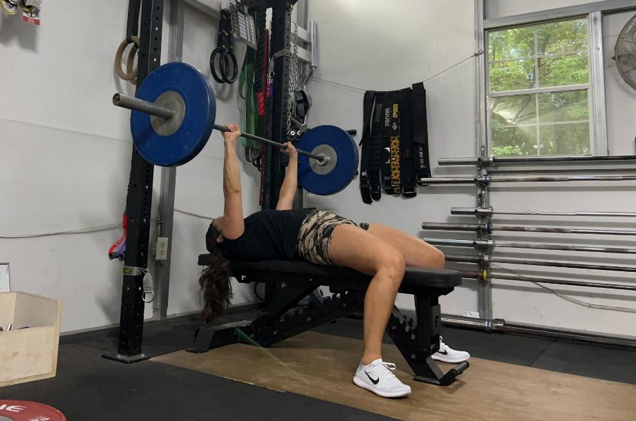 Woman in a garage gym benching using the Force USA Pro Series FID Bench