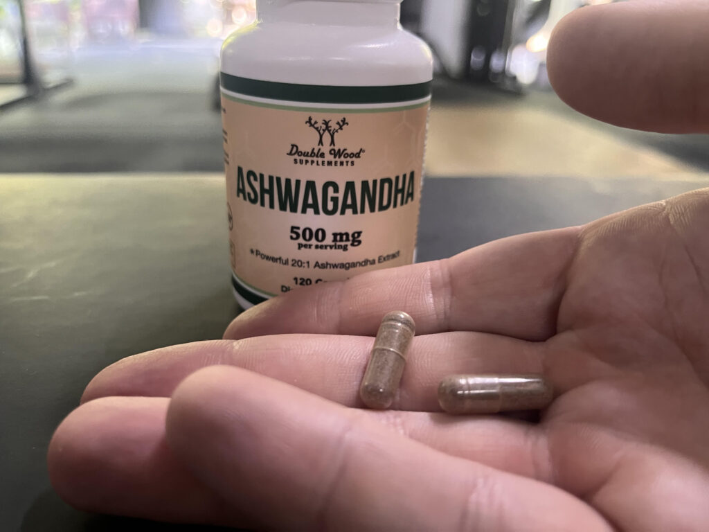 A hand holding a couple of Double Wood Ashwagandha pills in front of the container