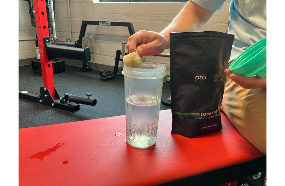 man scooping prohealth longevity greens into a clear shaker cup while sitting on a red bench