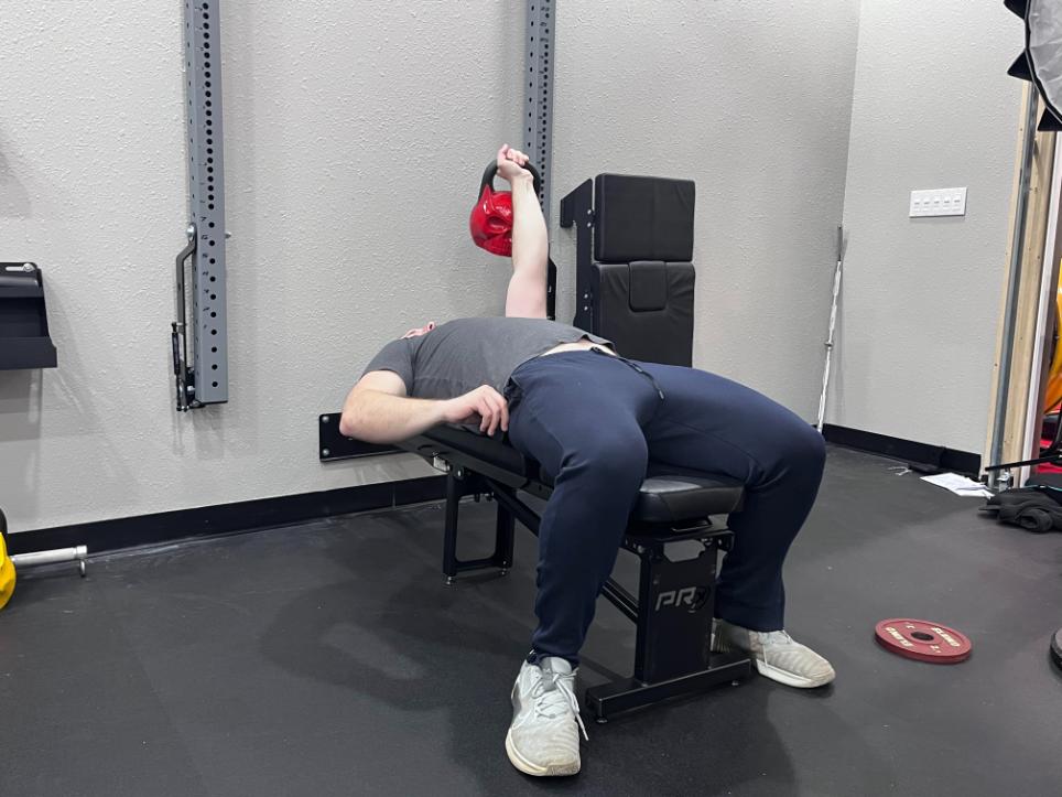 A man using a PRx Profile Folding Bench to perform single-arm kettlebell presses