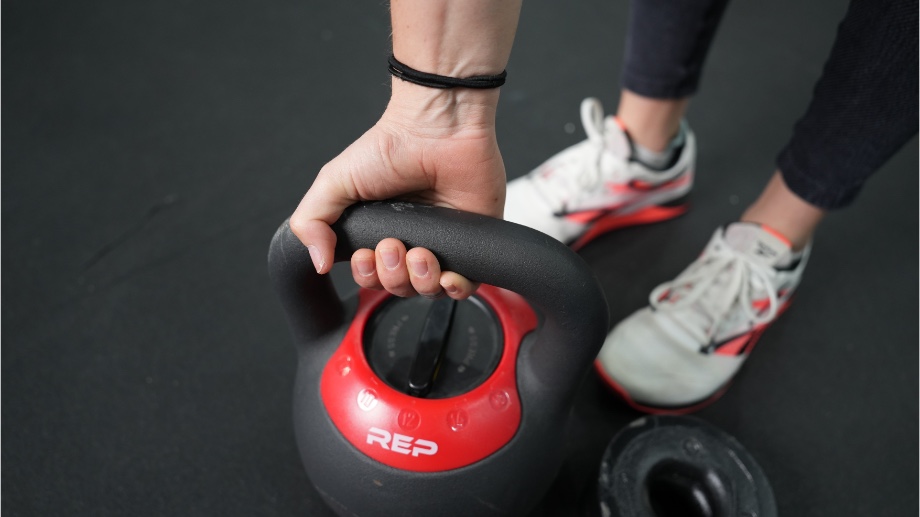 A hand holds a 16kg REP Fitness Adjustable Kettlebell.