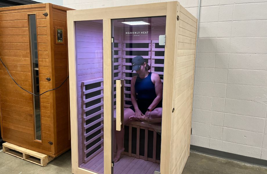 Woman wearing a baseball cap and workout clothes sitting inside the Heavenly Heat infrared sauna with chromotherapy lights