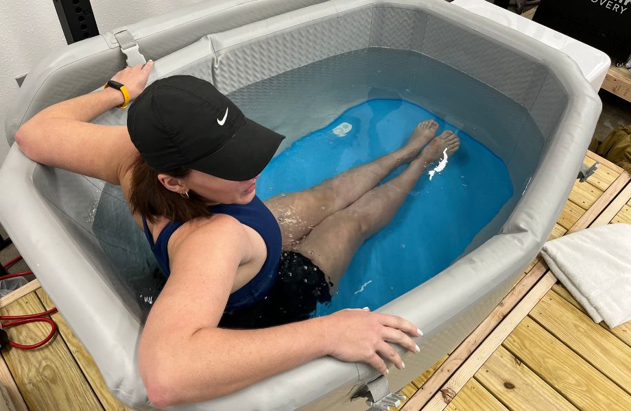 Woman in a black Nike baseball cap and workout attire sitting inside Plunge Air ice bath