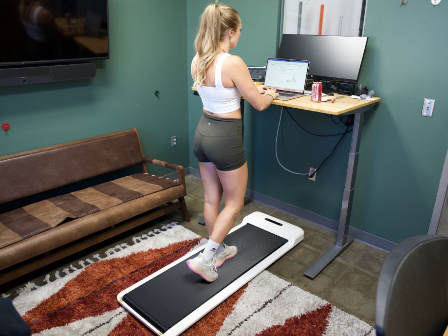 Blonde woman in workout clothes walking on a WalkingPad C2 while at a standing desk