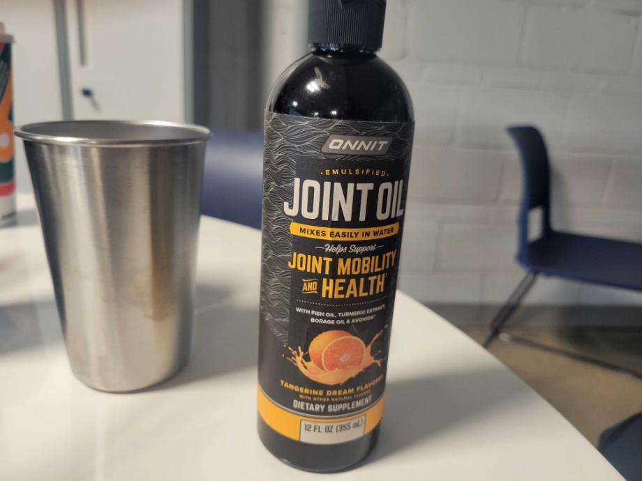 A bottle of Onnit Joint Oil is next to a stainless steel cup on a tabletop.