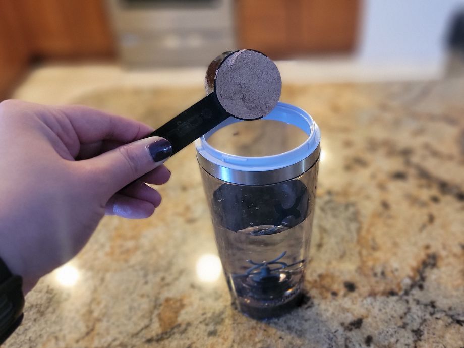 A person pours a scoop of protein powder into the PROMiXX Shaker Bottle